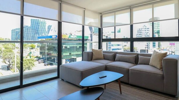 A modern living room with a sectional sofa, a coffee table, and large windows offering a city view.