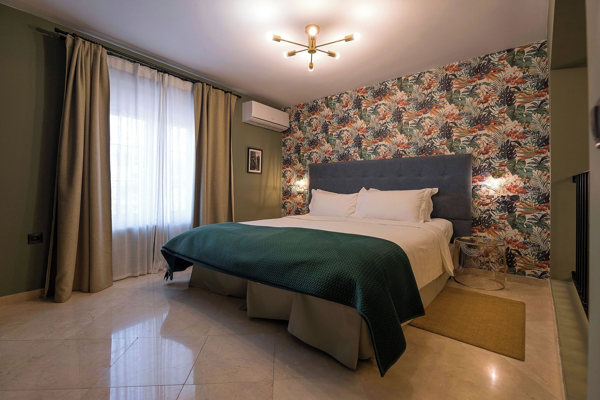 Une chambre à coucher avec un lit, des rideaux, un papier peint à motifs floraux, un appareil de climatisation et un luminaire au plafond.