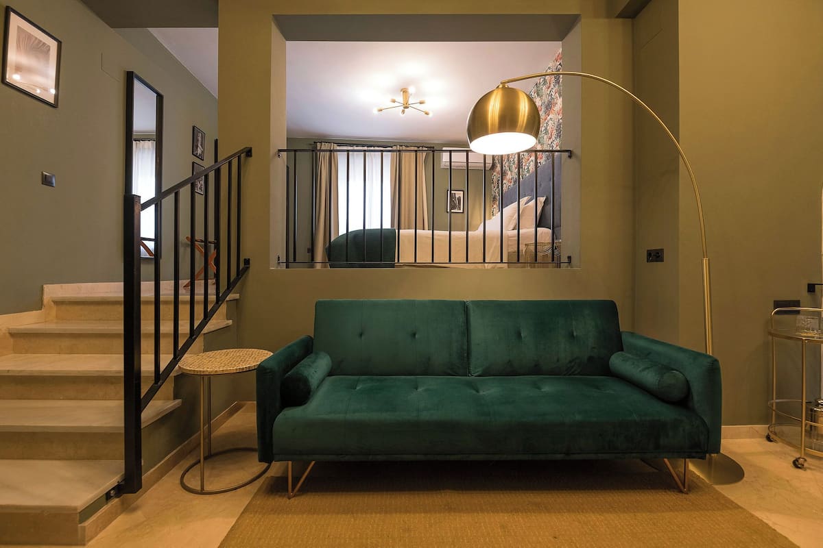 Uma sala de estar moderna com um sofá verde-turquesa, uma escada com corrimão preto e um abajur.