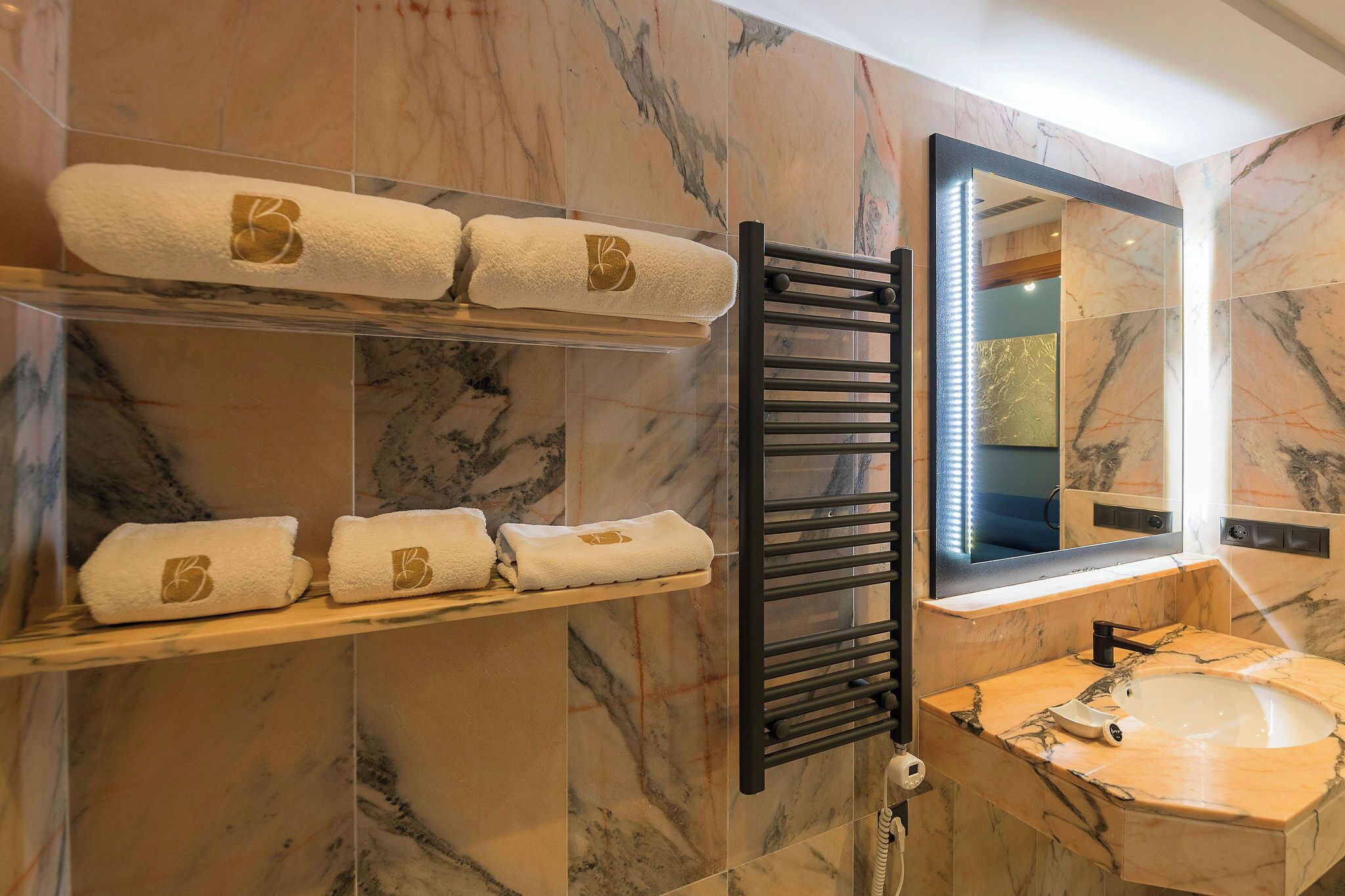 A bathroom with marble walls, a black towel rack, a mirror, and a sink.