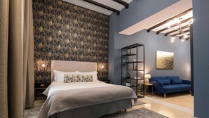 A modern bedroom with a large bed, a blue sofa, a patterned wallpaper, and a chandelier. - Boutique Suites (Arcos de la Frontera)