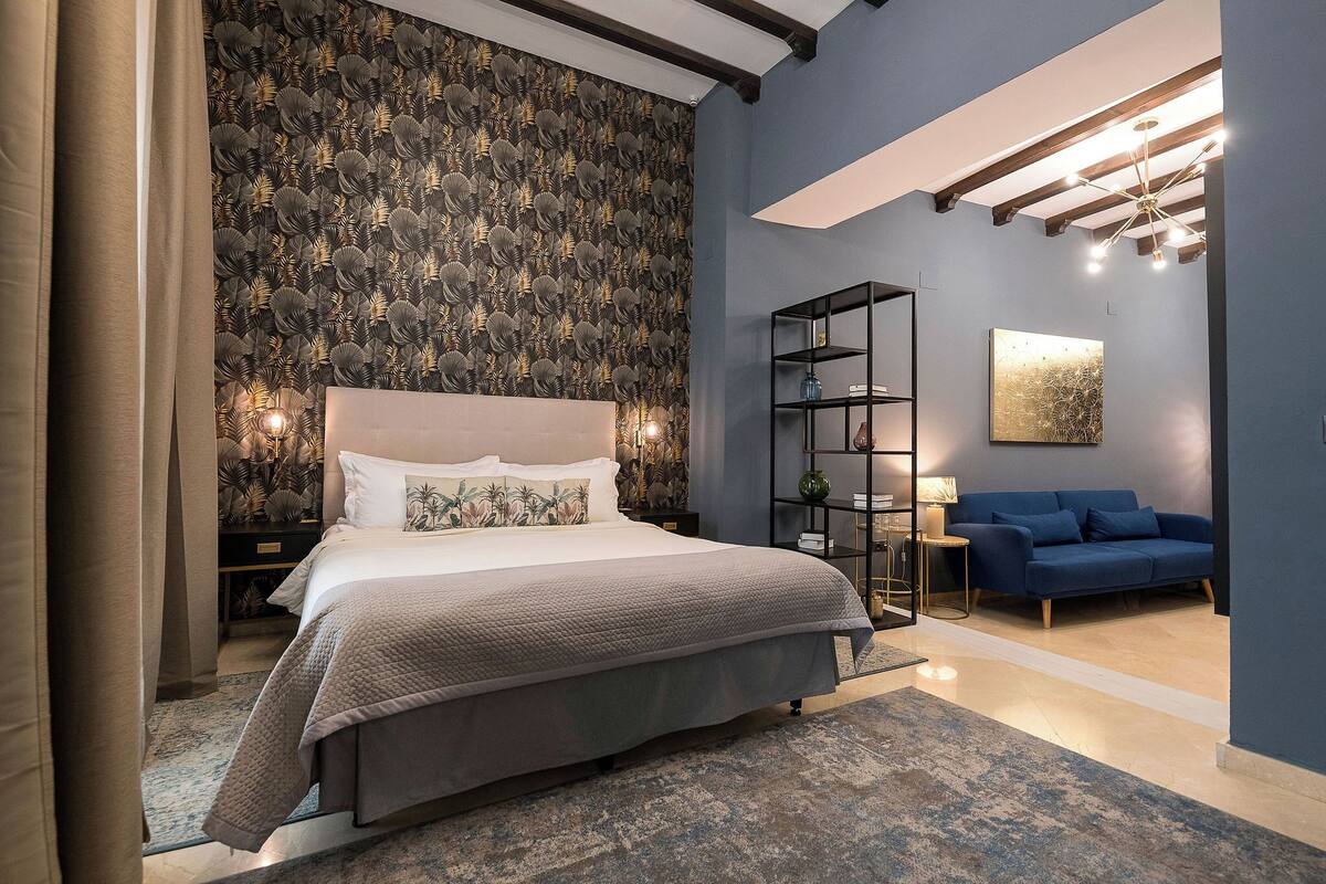 Um quarto moderno com uma cama grande, um sofá azul, papel de parede estampado e um candelabro.