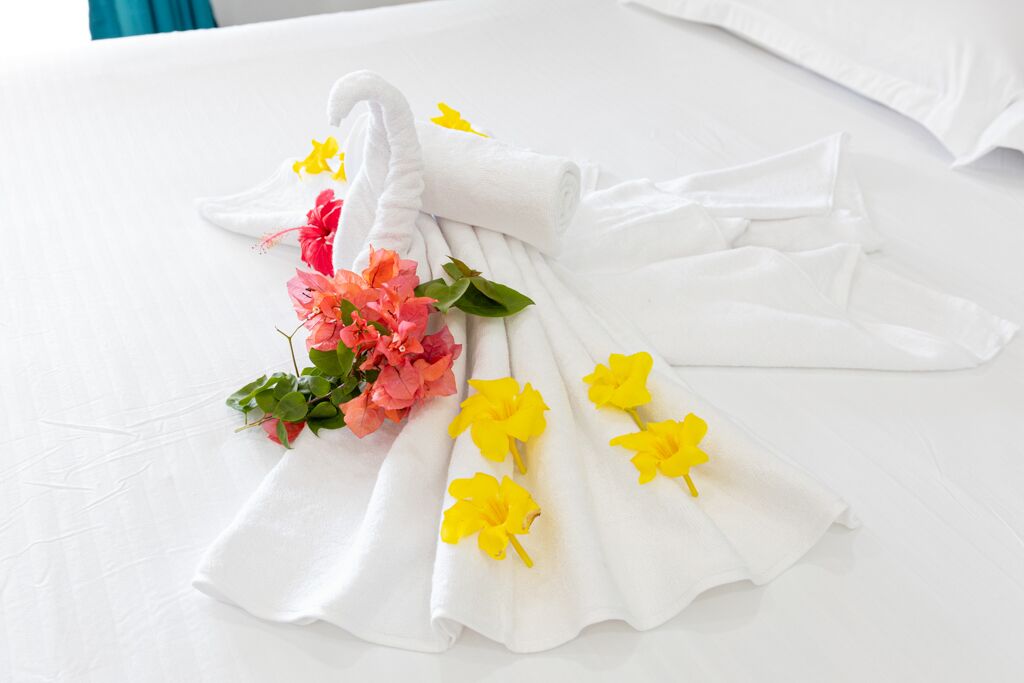 A neatly folded white towel with yellow flowers and pink flowers on a white bedspread.