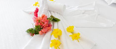 A neatly folded white towel with yellow flowers and pink flowers on a white bedspread.