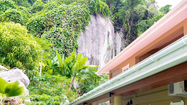 A house with a garden, a large rock, and a cliff in the background. - The Habitat Sesel (Mahé Island)