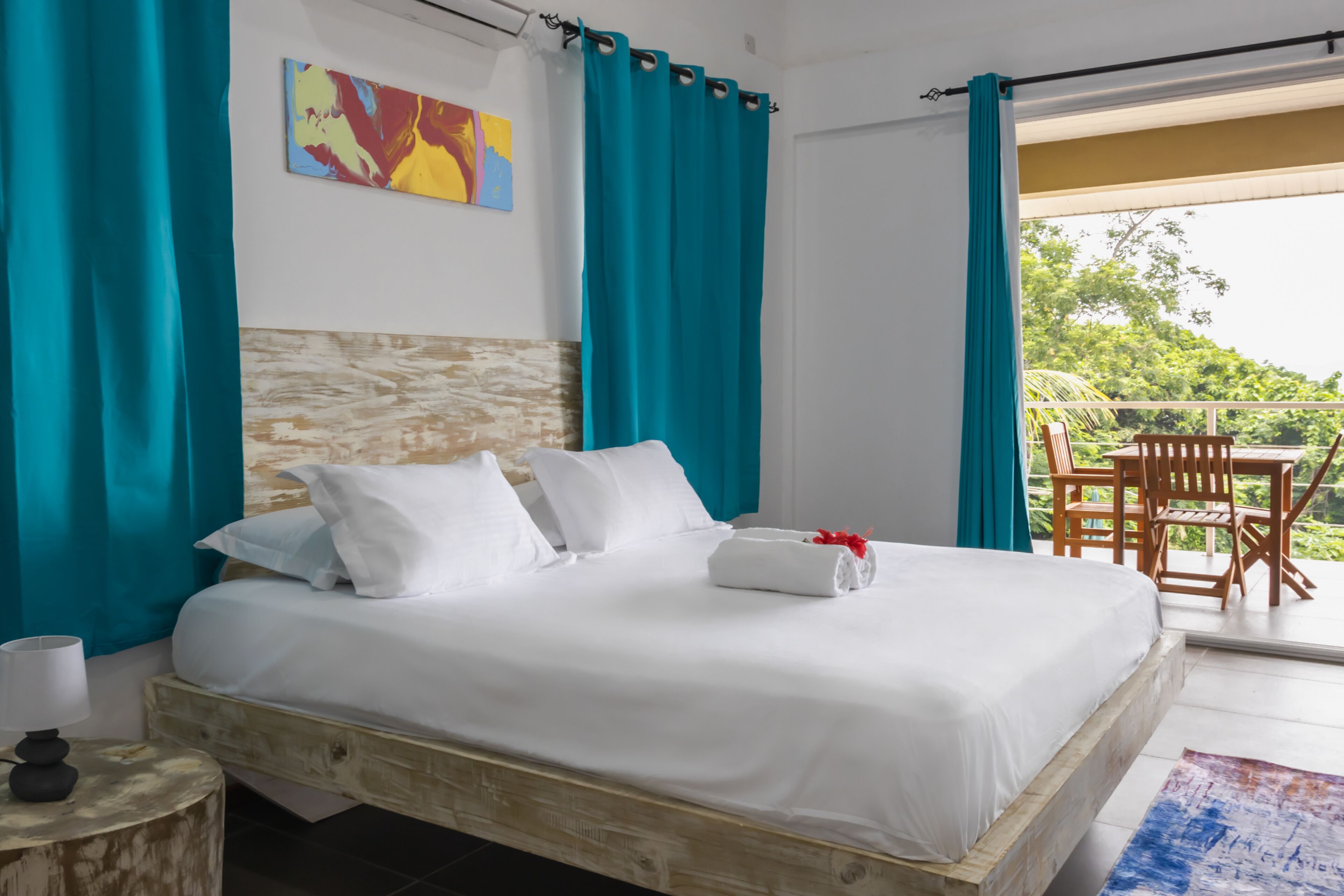 Ein Schlafzimmer mit Bett, Nachttisch, einem Gemälde und einem Balkon mit Sitzgelegenheiten.