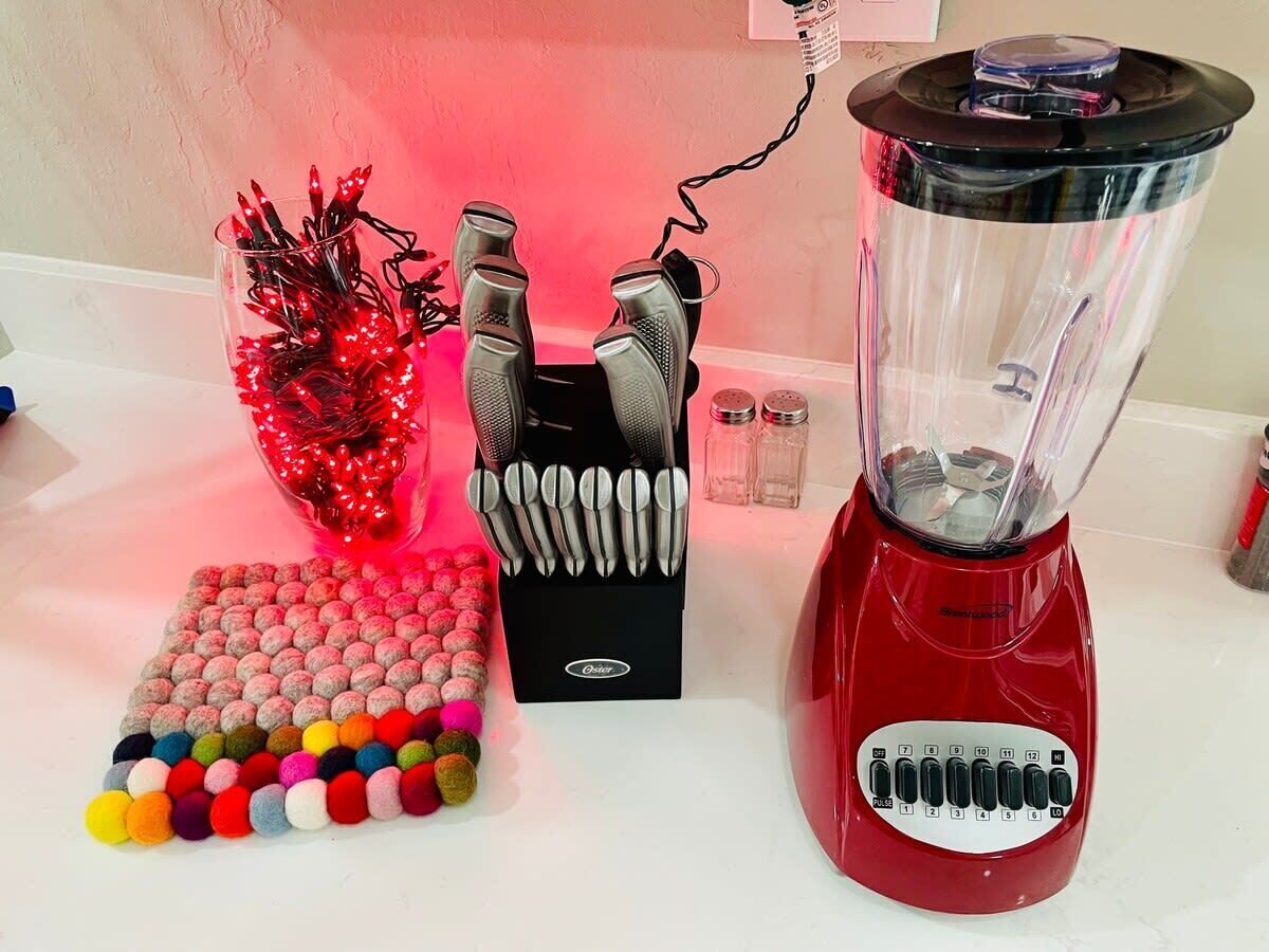 Un plan de travail de cuisine avec un mixeur rouge, un ensemble d’ustensiles de cuisine et une composition décorative de pompons colorés.