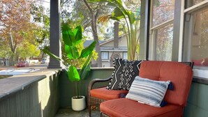 En fletstol med rød pude og et mønstret pudebetræk på en veranda med en potteplante.