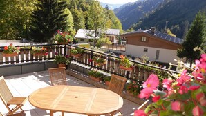 Eine Holzterrasse mit rundem Tisch und Stühlen, umgeben von Blumentöpfen und einem Holzzaun.