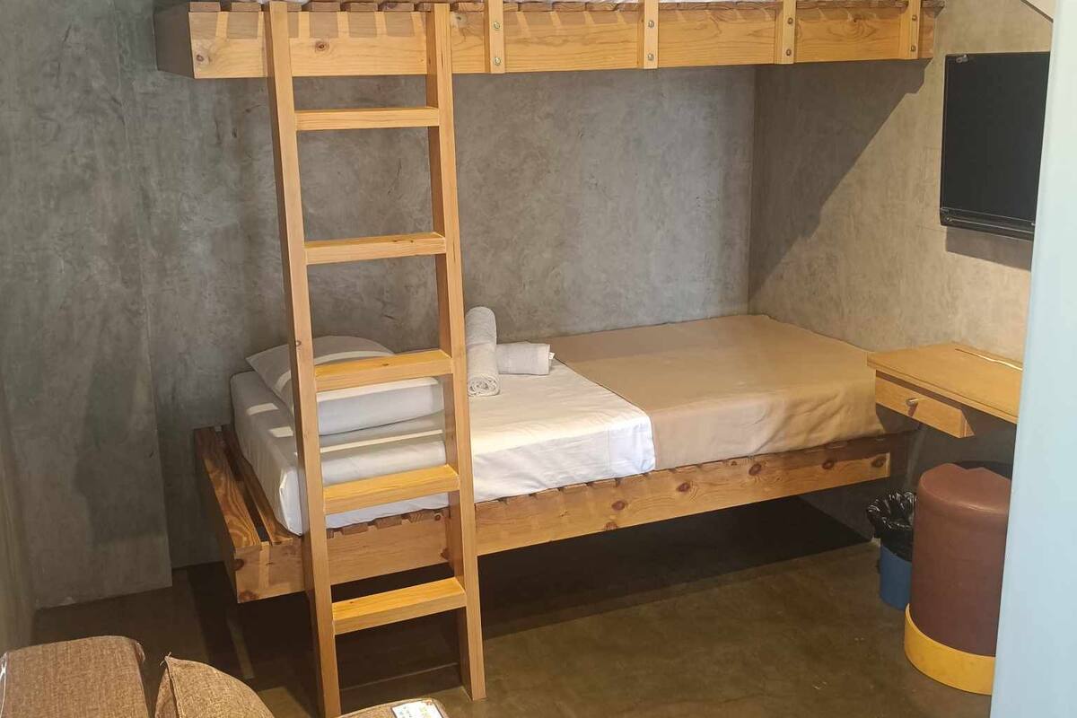 A bunk bed room with a wooden ladder, a desk, and a trash bin.