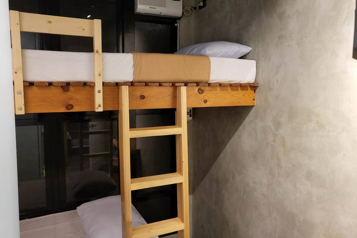 A bunk bed with a wooden ladder, a white pillow, and a wall-mounted air conditioner.