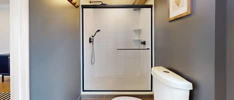 Une salle de bain moderne avec une douche à parois de verre, des toilettes blanches et une petite étagère contenant des articles de toilette.