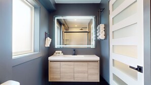 A modern bathroom with a large mirror, a white sink, and a wooden vanity. - The Surf Club (Ocean City)