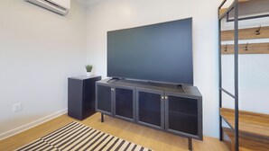 A modern living room with a flat-screen TV mounted on a black entertainment unit, a small potted plant, and a striped rug on a wooden floor. - The Surf Club (Ocean City)