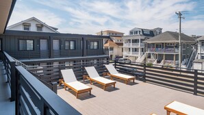 A rooftop deck with lounge chairs and a wooden table, overlooking a residential area with houses and a staircase. - The Surf Club (Ocean City)