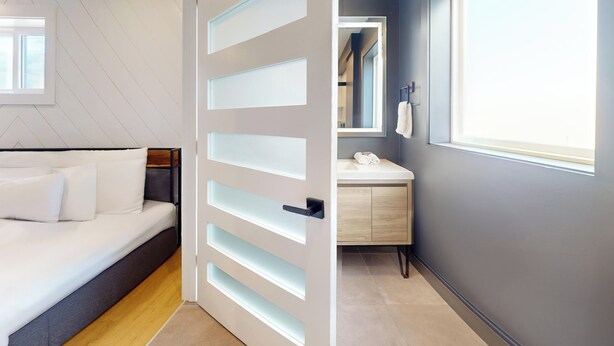 A modern bedroom with a bed, a bedside table, and a wardrobe. - The Surf Club (Ocean City)