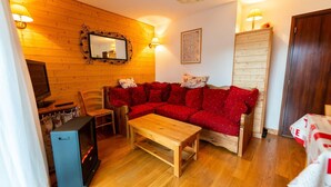 A cozy living room with a red sofa, wooden floor, a small table, a TV, and a cabinet. - Warm 29m² with balcony and lake view (Gérardmer)