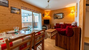 A wooden interior with a dining area, a sofa, a TV, and a fireplace. - Warm 29m² with balcony and lake view (Gérardmer)