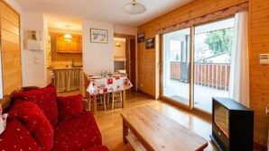 A cozy living room with a red sofa, a wooden coffee table, and a TV. There's a dining area with a table and chairs, and a kitchen in the background. - Warm 29m² with balcony and lake view (Gérardmer)