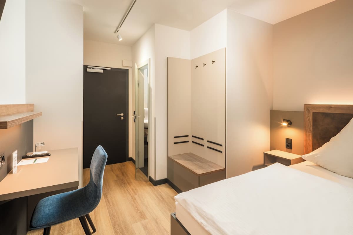 A modern hotel room with a bed, desk, chair, and a walk-in closet.