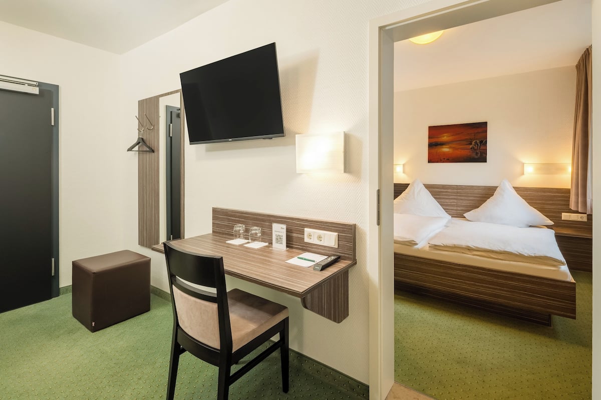 A hotel room with a bed, a desk, a chair, a TV, and a painting on the wall.