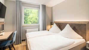 Una habitació d'hotel amb dos llits, una taula de treball, una cadira, un televisor i una finestra amb cortines.