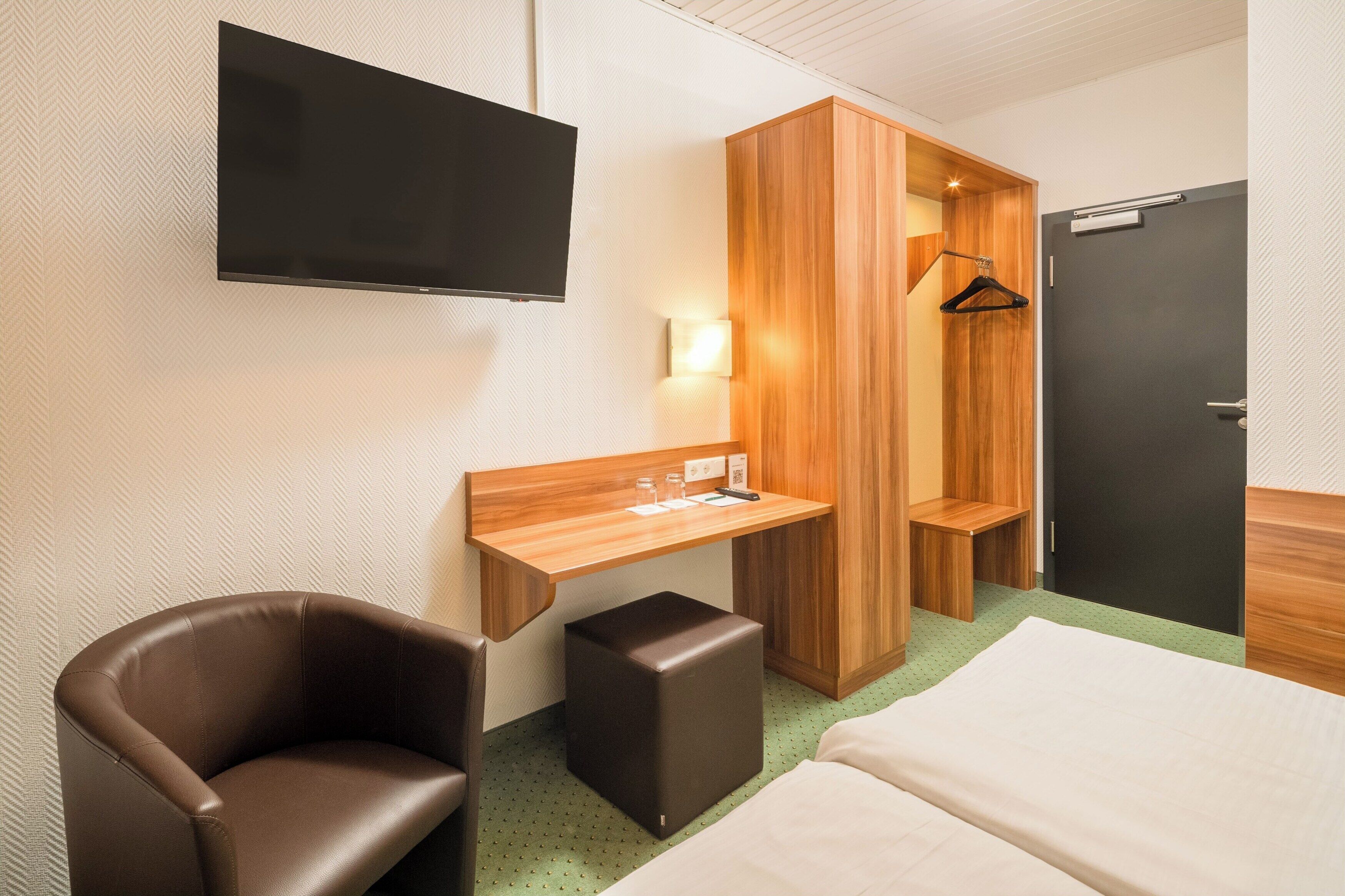 A hotel room with a bed, a desk, a chair, a TV, a wardrobe, and a door.
