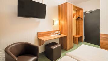 A hotel room with a bed, a desk, a chair, a TV, a wardrobe, and a door.
