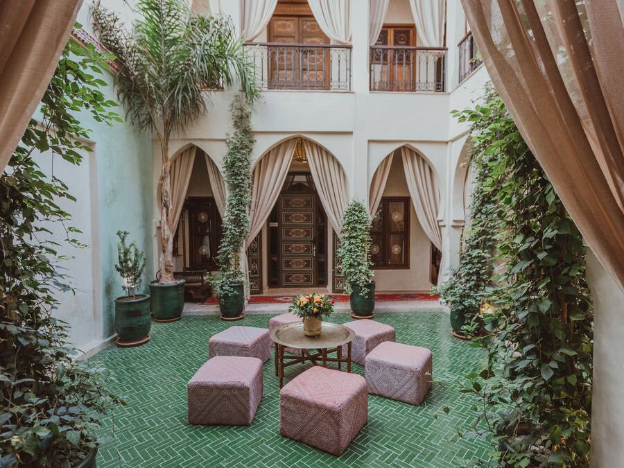 A courtyard with a green tiled floor, a round table with a vase of flowers, and several cushioned seating areas.