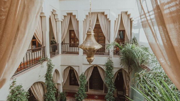 A courtyard with arches, a hanging light fixture, and plants. - Riad El Hara (Marrakech)