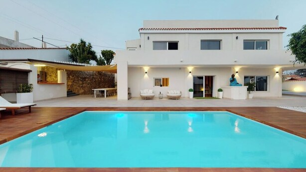 A modern two-story house with a swimming pool, outdoor seating, and a stone wall.