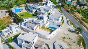 Ein moderner Wohnkomplex mit mehreren miteinander verbundenen Häusern, einem Schwimmbad und einer nahegelegenen Straße.