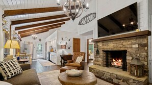 A spacious living room with a stone fireplace, leather armchair, and a chandelier.