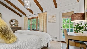 A bedroom with a large bed, wooden beams, a desk, and a window with curtains.