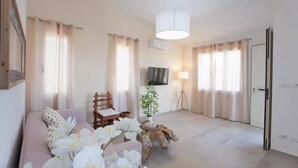 A living room with a sofa, a chair, a lamp, and a TV on the wall. - Pina Apartment - Relax & Comfort  (Budoni)
