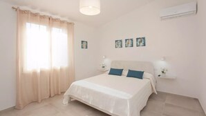 A bedroom with a bed, curtains, wall-mounted air conditioning, and artwork. - Pina Apartment - Relax & Comfort  (Budoni)