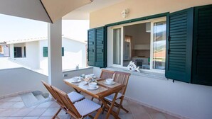 A balcony with a table set for four, a chair, and a decorative fish sculpture. - Pina Apartment - Relax & Comfort  (Budoni)