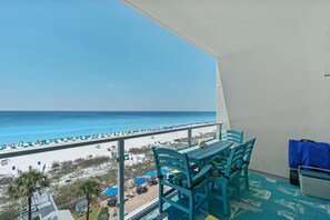 En balkon med udsigt over stranden, et bord, stole og en kuffert.