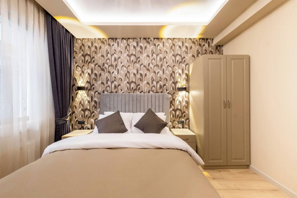 A modern hotel room with a large bed, a wardrobe, and a patterned wallpaper.