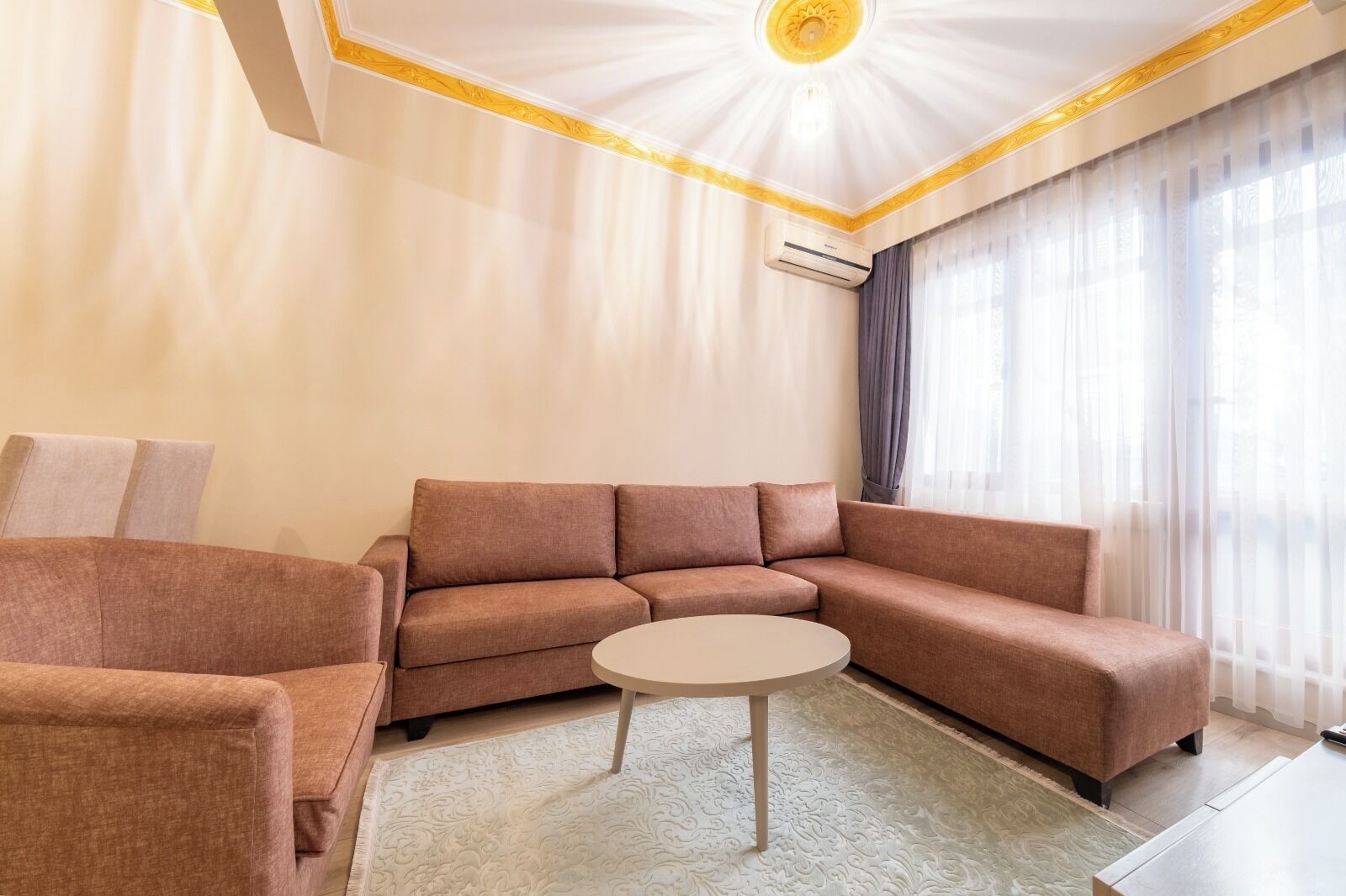 Un salon moderne avec un canapé d’angle, une table basse ronde et une grande fenêtre agrémentée de rideaux.