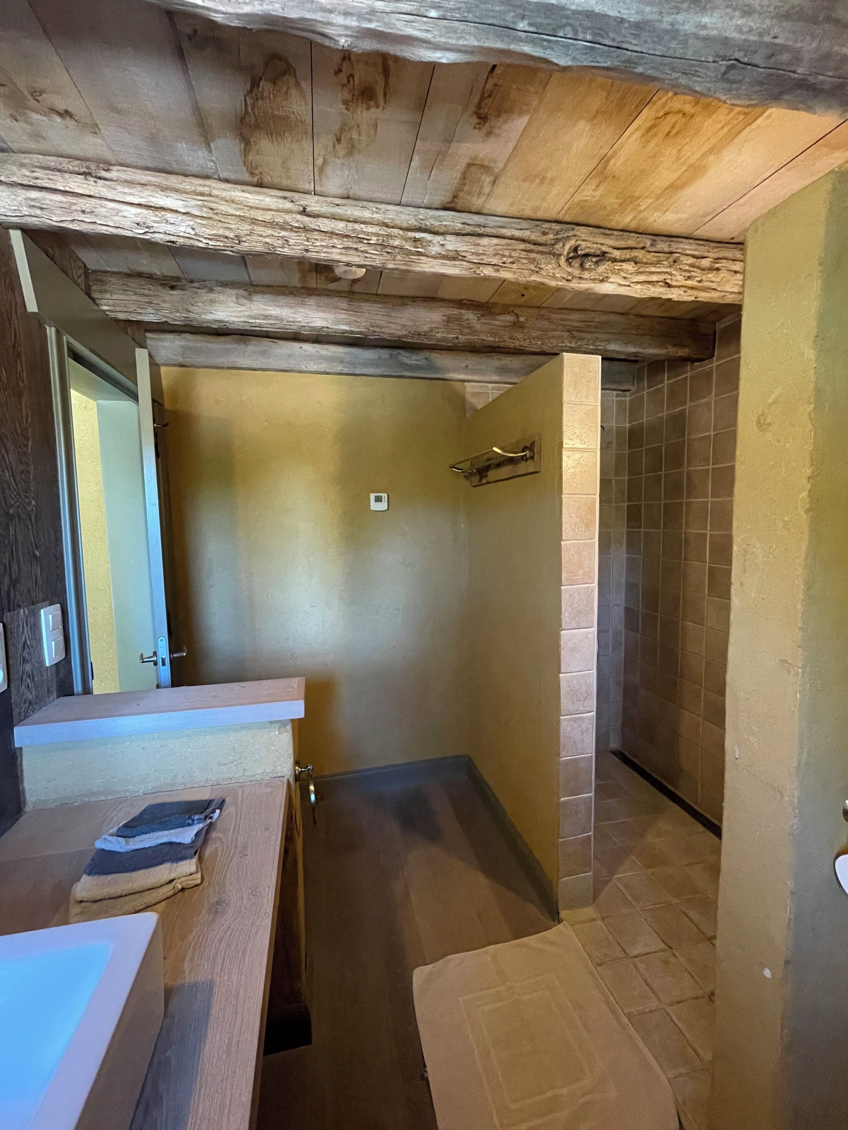 Ein Badezimmer mit Holzboden, einer Duschkabine mit gefliesten Wänden und einem Waschbecken mit Handtuch.