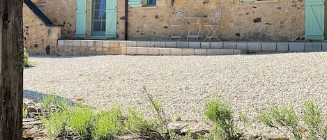 A stone building with a gravel driveway, a balcony with metal railings, and a small table and chair set outside.
