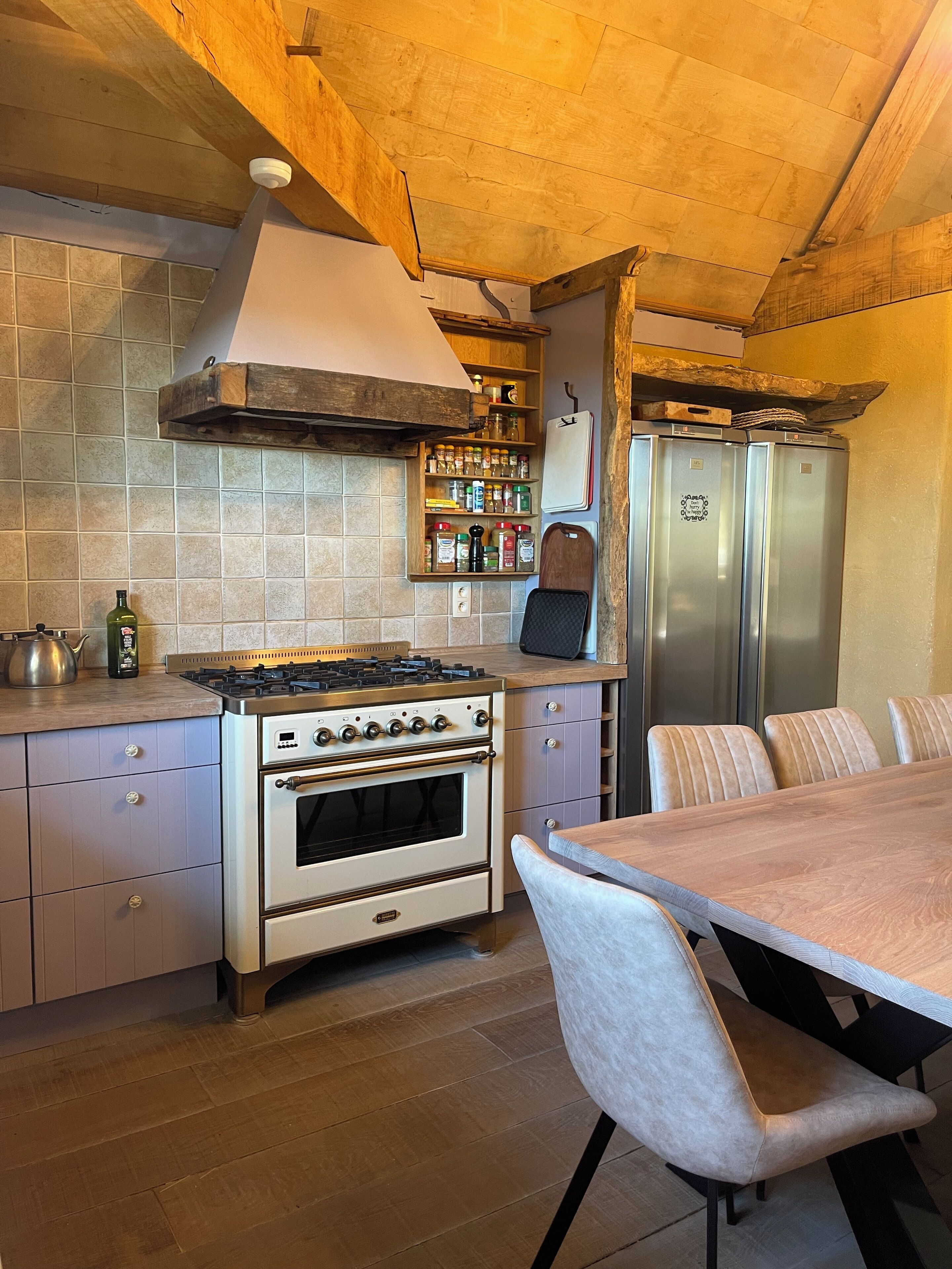 A kitchen with a gas stove, oven, and a built-in refrigerator. There is a wooden shelf with spices and a kettle on the counter.