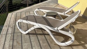 Una terraza con dos sillones blancos y una mesita, con vistas a un paisaje pintoresco con campos y colinas al fondo.