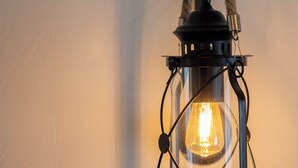 Un farol negro con asa de cuerda colgando frente a una pared lisa.