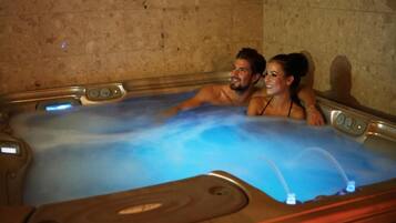 A couple in a hot tub with a control panel and a tiled wall.