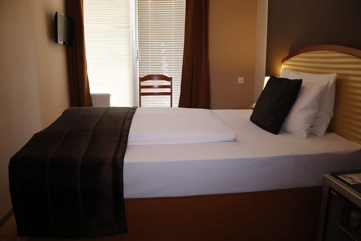 Ein Hotelzimmer mit Bett, Holz-Kopfteil, Wand-Fernseher und Fenster mit Jalousien.