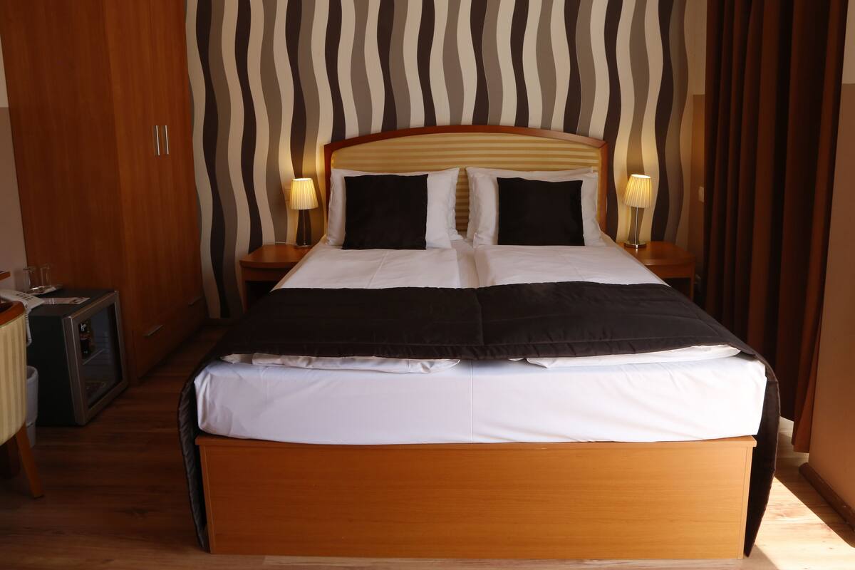 Ein Hotelzimmer mit einem großen Bett, zwei Nachttischen mit Lampen, einem Kleiderschrank und einer gestreiften Wand.