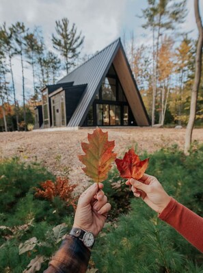 Une personne tenant deux feuilles devant un bâtiment moderne doté d’un toit triangulaire.