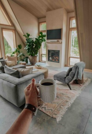 A cozy living room with a sofa, a coffee table, a fireplace, and a large window. - *NEW* Luxury A-Frame by Sunday River w/ hot tub (Bethel)